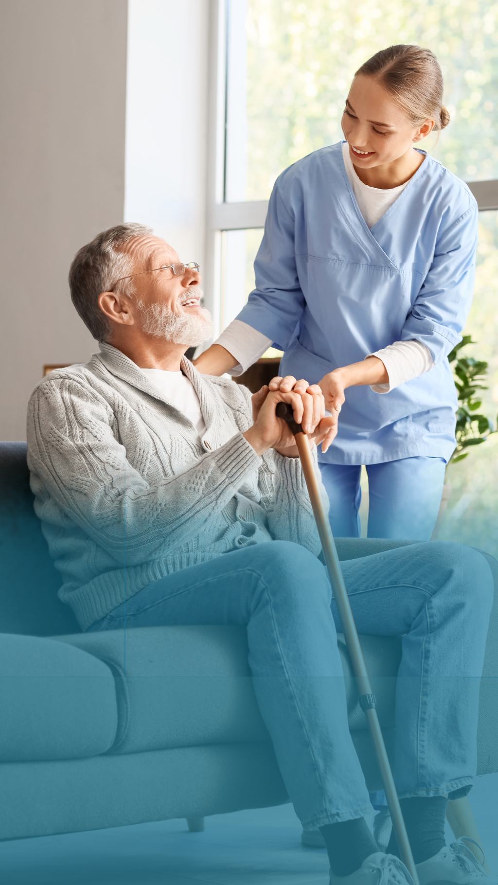 A care worker helping an older man to his feet from a sofa, steadying him as he takes his walking stick.
