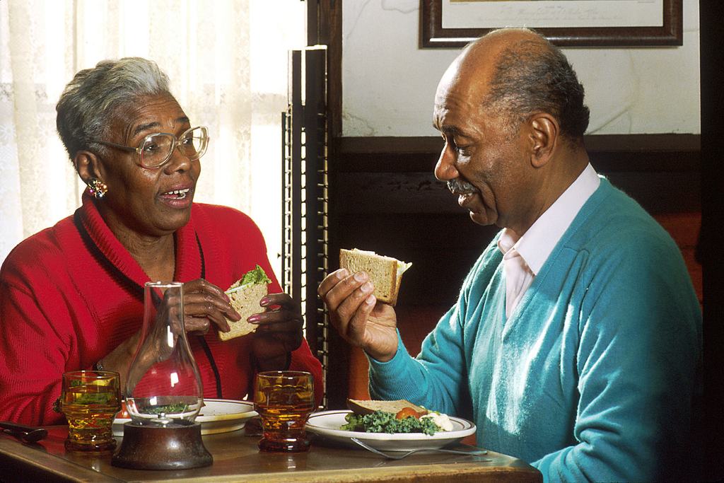 An older couple sitting at a table at home, eating a light meal together.