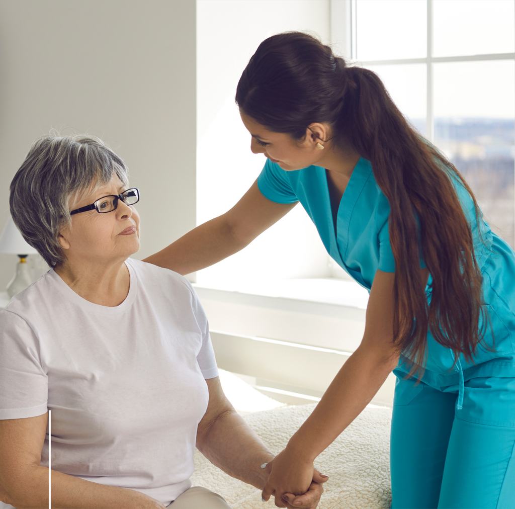A care worker sitting beside an older woman at home, holding her hand.