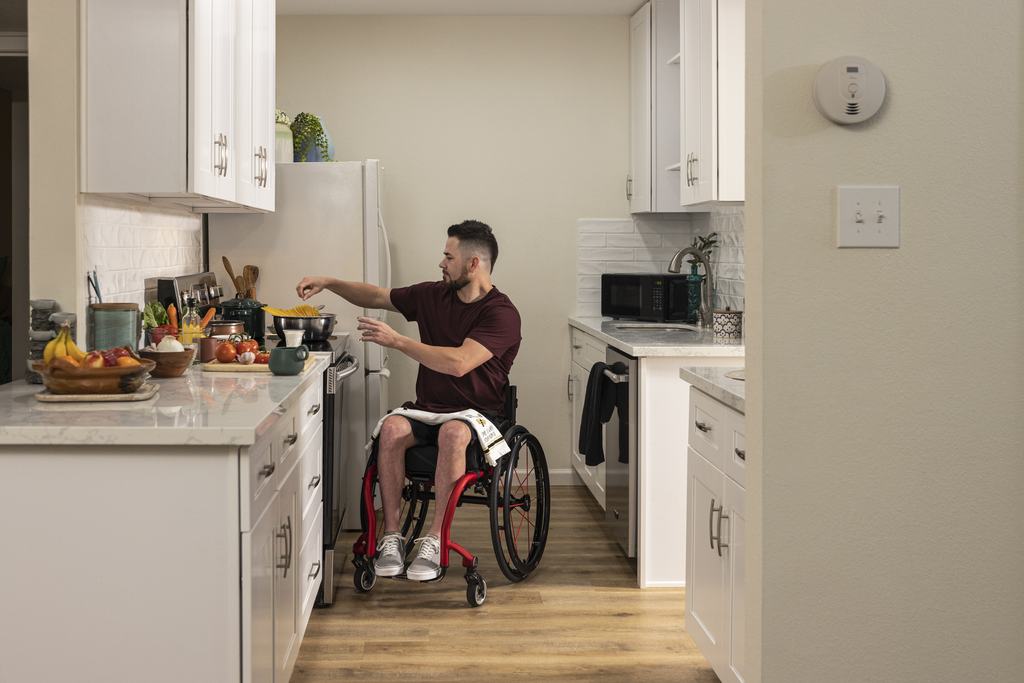 A man in a wheelchair cooking a meal unassisted at the hob in his own kitchen.
